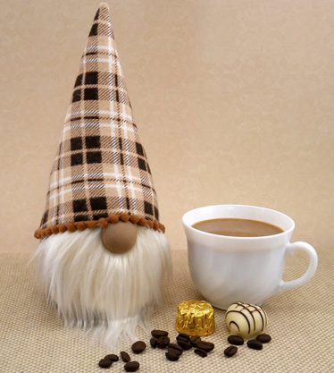 Gonk with cream color beard and brown tan plaid fabric next to a cup of coffee